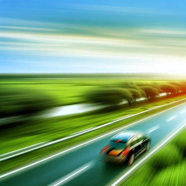 Snel bewegende auto op zonovergoten snelweg Een auto die snel over een zonverlichte snelweg rijdt, omringd door vredige heuvels.